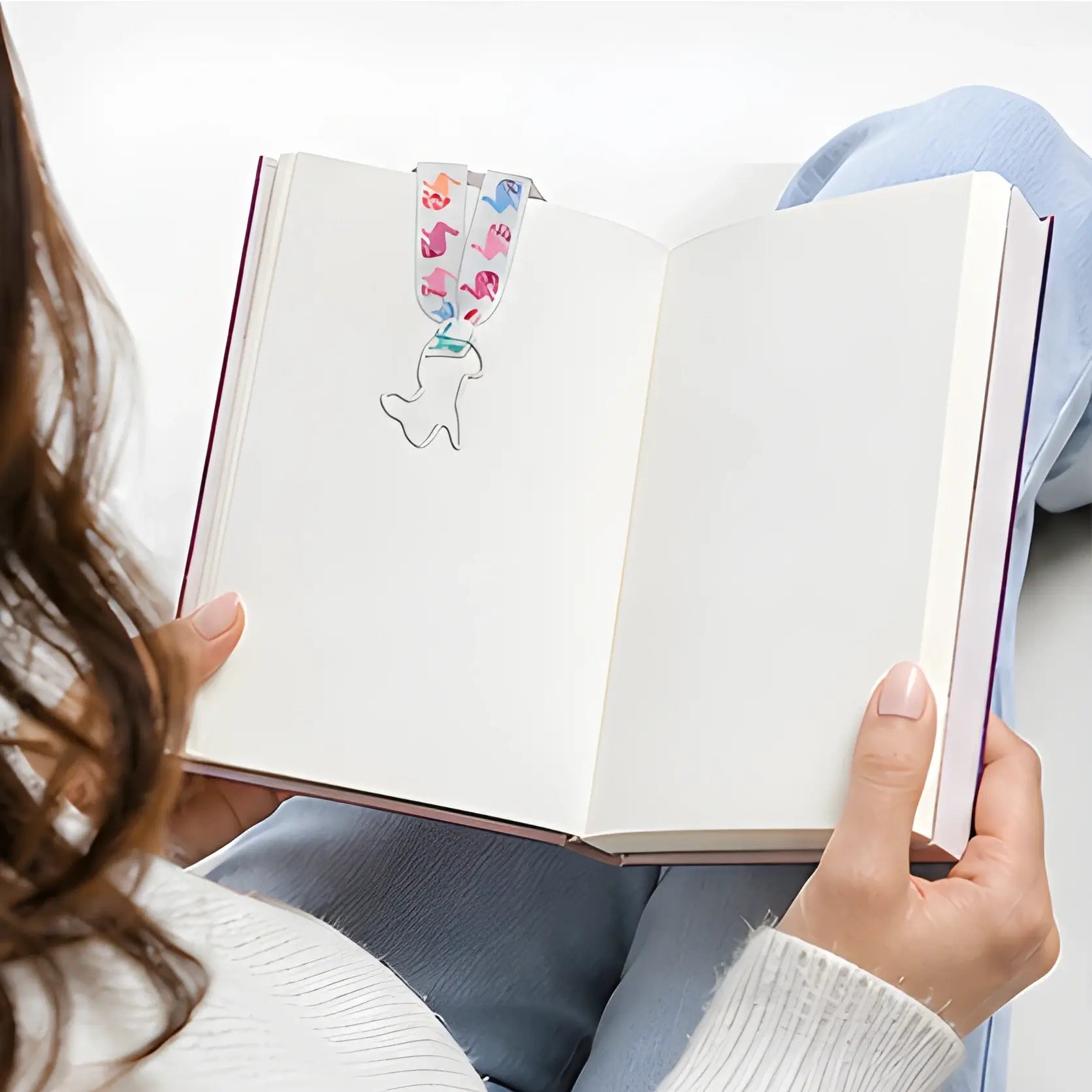 Person holding an open book with a colorful whale-shaped bookmark.