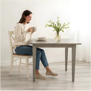 The Windermere Square Dining Table - SearchPify - Woman sitting at a dining table holding a cup, with a vase of flowers on the table.