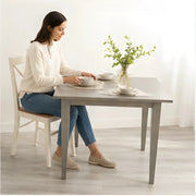 The Windermere Square Dining Table - SearchPify - Woman sitting at a dining table setting plates with a vase of flowers on the table.